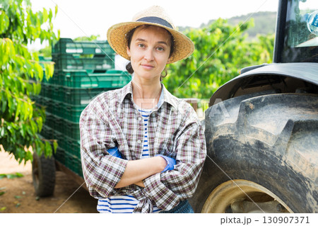 Portrait of female farmer stands next to tractor in an orchard 130907371