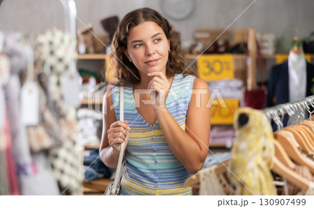 Young woman chooses a set of clothes for the summer. Visitor to the boutique examines new summer collection of clothes Young woman chooses a set of clothes for the summer. Visitor to the boutique examines new summer collection of clothes 130907499