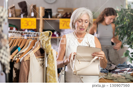 Happy mature woman choosing handbag in clothing store Happy mature woman choosing handbag in clothing store 130907560