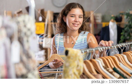 Positive young woman choosing something for summer in clothing store 130907657