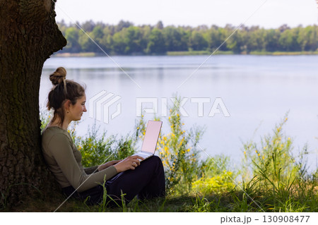 A Young Woman Enjoys Working Remotely by a Serene and Calm Lake During a Beautiful Day 130908477