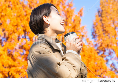 紅葉を楽しみながらホットドリンクを飲む女性　ライフスタイルイメージ 130908513