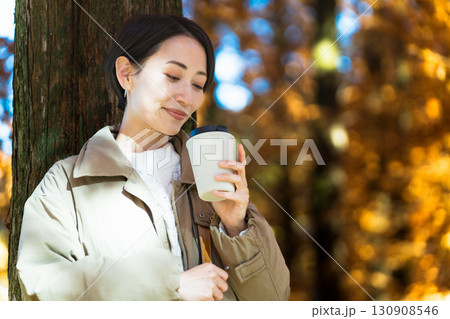 紅葉を楽しみながらホットドリンクを飲む女性　ライフスタイルイメージ 130908546