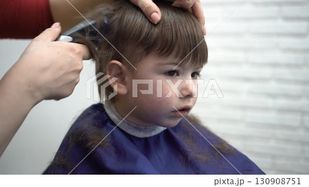 three-year-old sitting in barber chair watching the mirror during a haircut 130908751