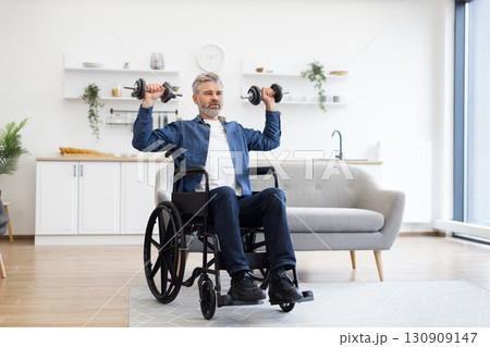 Mature Caucasian man in wheelchair lifting dumbbells during fitness activity at home, showcasing positivity, strength, and resilience. Bright and modern environment with natural lighting 130909147