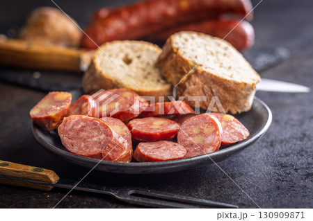 Smoked sliced sausages and bread on plate on black table. Smoked sliced sausages and bread on plate on black table. 130909871
