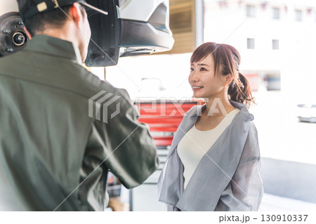 整備工場でマイカーのメンテナンス,車検の説明を受ける女性客と整備士の男性スタッフ 整備工場でマイカーのメンテナンス,車検の説明を受ける女性客と整備士の男性スタッフ 130910337