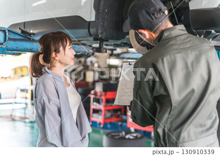 整備工場でマイカーのメンテナンス,車検の説明を受ける女性客と整備士の男性スタッフ 整備工場でマイカーのメンテナンス,車検の説明を受ける女性客と整備士の男性スタッフ 130910339