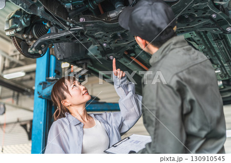自動車の下回りで整備士,メカニックから説明を受ける女性客 自動車の下回りで整備士,メカニックから説明を受ける女性客 130910545
