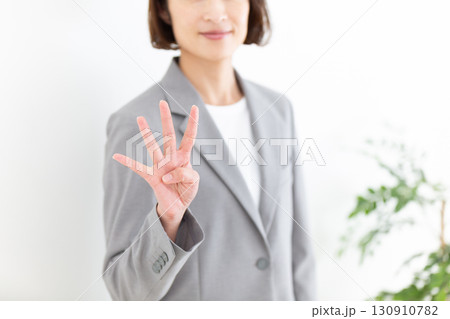 指を4本立てるグレーのスーツ姿のミドル女性ビジネスウーマン 130910782