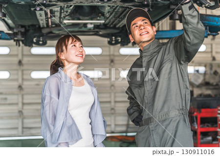 自動車の下回りで整備士,メカニックから説明を受ける女性客 自動車の下回りで整備士,メカニックから説明を受ける女性客 130911016