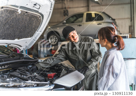 車のエンジンルームで女性客に説明,解説をする整備士,メカニックの男性スタッフ 車のエンジンルームで女性客に説明,解説をする整備士,メカニックの男性スタッフ 130911130
