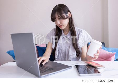 リビングでマグカップを手にPC作業をする真剣な表情の日本人女性 リビングでマグカップを手にPC作業をする真剣な表情の日本人女性 130911291