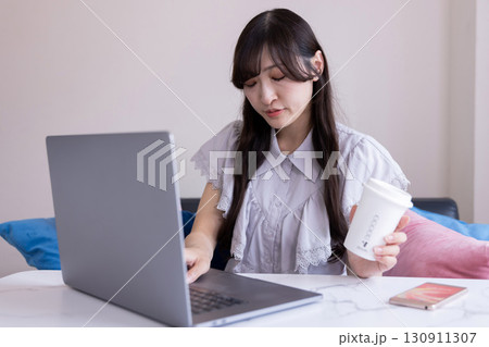リビングでマグカップを手にPC作業をする真剣な表情の日本人女性 リビングでマグカップを手にPC作業をする真剣な表情の日本人女性 130911307