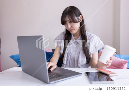 リビングでマグカップを手にPC作業をする真剣な表情の日本人女性 リビングでマグカップを手にPC作業をする真剣な表情の日本人女性 130911332