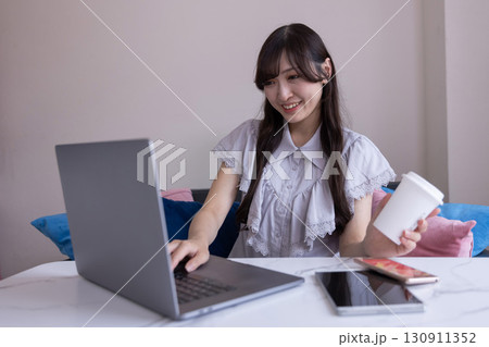 リビングでマグカップを手にPC作業をする真剣な表情の日本人女性 リビングでマグカップを手にPC作業をする真剣な表情の日本人女性 130911352