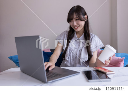 リビングでマグカップを手にPC作業をする真剣な表情の日本人女性 リビングでマグカップを手にPC作業をする真剣な表情の日本人女性 130911354