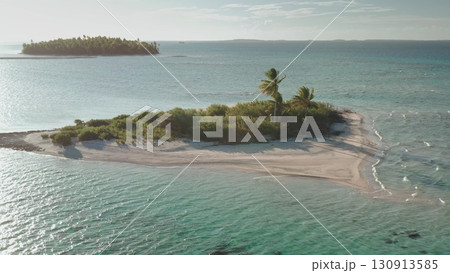 Aerial view capturing a small desert island with lush palm trees and vegetation, surrounded by turquoise waters in French Polynesia's tropical paradise Aerial view capturing a small desert island with lush palm trees and vegetation, surrounded by turquoise waters in French Polynesia's tropical paradise 130913585