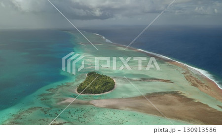 Aerial view of Fakarava Atoll in French Polynesia, featuring a lush motu surrounded by a vibrant turquoise lagoon and a shallow coral reef under a dramatic sky Aerial view of Fakarava Atoll in French Polynesia, featuring a lush motu surrounded by a vibrant turquoise lagoon and a shallow coral reef under a dramatic sky 130913586