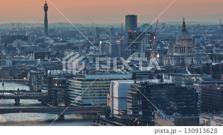 United Kingdom, London: Aerial view capturing London's iconic skyline at sunset, featuring BT Tower, St. Paul's Cathedral, and illuminated buildings along the River Thames. Drone flight 130913628