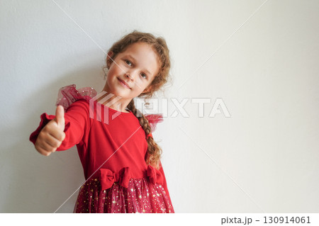A cheerful girl in a sparkly red dress gives a thumbs up and smiles confidently 130914061