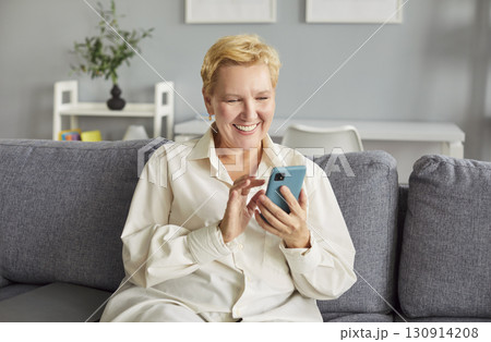Cheerful mature woman radiating joy scrolls through her mobile phone, enjoying quiet moment. 130914208