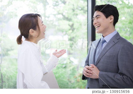新緑の窓際でビジネスで会話するシーン　女性上司と男性の部下	 130915656