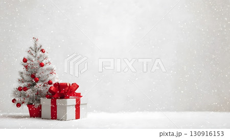 A small white Christmas tree with red ornaments and a gift box stand on snow, creating a bright festive background. 130916153