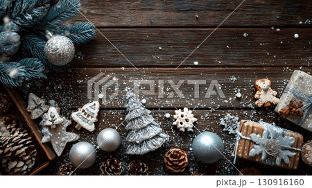 Rustic Christmas background features sparkling ornaments, frosted pine, holiday gifts, cookies, and snow on wood. 130916160