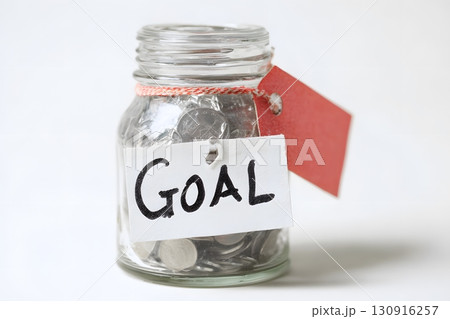 Glass jar with money accumulating towards a goal. Glass jar with money accumulating towards a goal. 130916257