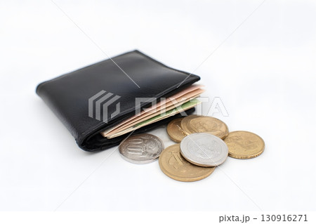 A black wallet holds money with coins spread out on a white surface. 130916271