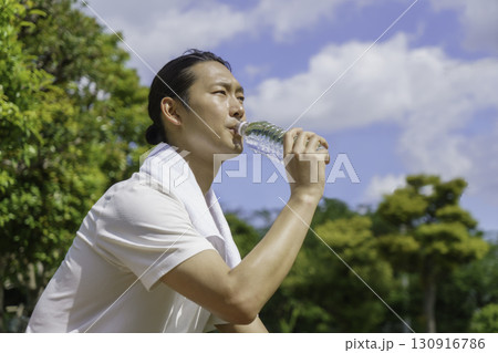 公園のベンチに座って水分補給をする若い男性 公園のベンチに座って水分補給をする若い男性 130916786