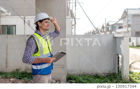 Construction supervisor in safety gear observe the development of new home at a worksite during daylight. He note detail and monitor progress on tablet computer, ensuring safety standard. 130917394