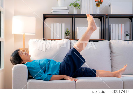 Senior asian woman practice stretch leg for treatment knee pain lying on sofa in living room. 130917415