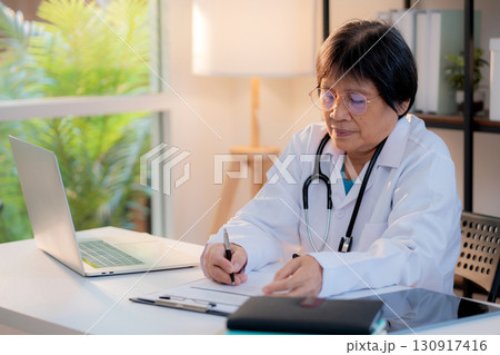 Senior asian doctor writing prescription or document on clipboard in clinic office. 130917416