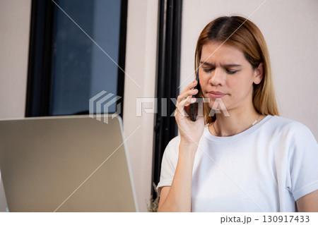 Young caucasian businesswoman working on laptop computer while talking on smartphone. Young caucasian businesswoman working on laptop computer while talking on smartphone. 130917433