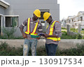 Two construction worker in a helmet and safety vest review plan on tablet at a building site. They focus intently on their task while discussing project detail. 130917534