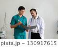 Two healthcare worker in scrub review patient information in a bright, well-equipped hospital room. Medical equipment is visible in the background. 130917615