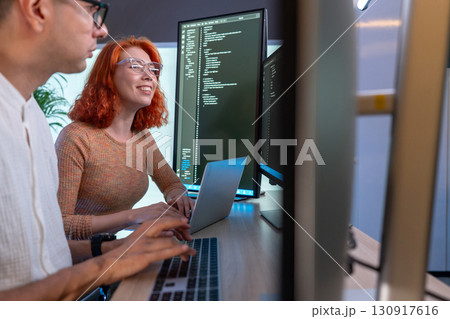 Two developer focus on coding at their desk, surrounded by multiple computer screen displaying line of code in a contemporary workspace, enhancing teamwork and creativity. Two developer focus on coding at their desk, surrounded by multiple computer screen displaying line of code in a contemporary workspace, enhancing teamwork and creativity. 130917616