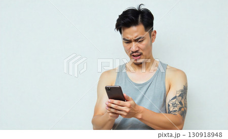 スマホを見て顔をしかめるタトゥーが入った男性 130918948