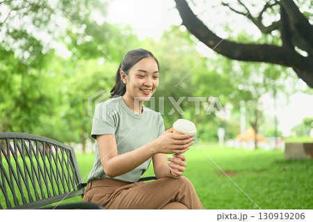 Happy young woman in casual outfit enjoying a hot drink while sitting outside in a peaceful natural 130919206
