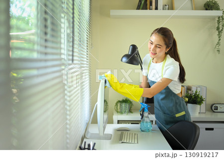 Young woman cleaning a computer monitor with a microfiber cloth and spray bottle in a bright office Young woman cleaning a computer monitor with a microfiber cloth and spray bottle in a bright office 130919217