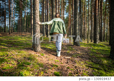 Back view of woman walking through forest between pine trees and foraging for mushrooms in autumn 130919437