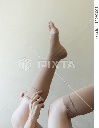 Woman putting on compression stockings in bedroom to prevent varicose veins. Swelling and leg pain, medical hosiery for circulation and vein health 130920014