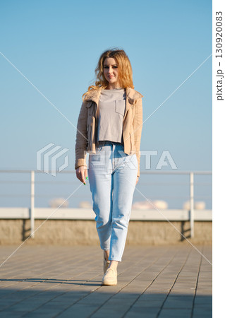 Model walks confidently on a sunny day in urban setting wearing casual style 130920083