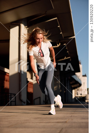 Athletic young woman sprinting outdoors in urban setting under bright sunlight 130920220