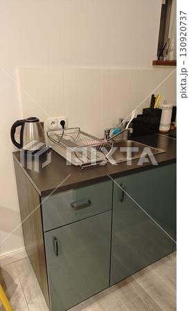 Modern small kitchen corner with metal kettle, sink and dish rack. Concept of compact and functional cooking area in a contemporary home 130920737