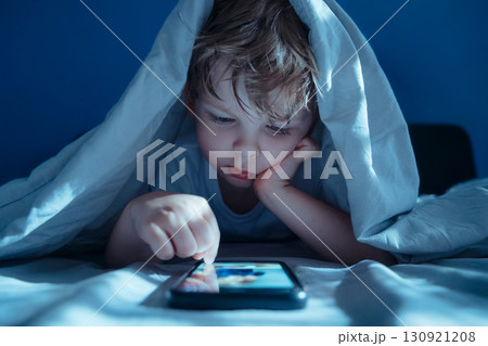 Child under blanket staring at smartphone at night Child under blanket staring at smartphone at night 130921208