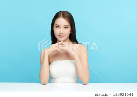A beautiful young Asian woman with clean, fresh skin against a blue background. Skincare, facial treatment, cosmetology, beauty, and spa. An elegant portrait of an Asian woman. 130921541