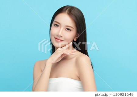 A beautiful young Asian woman with clean, fresh skin against a blue background. Skincare, facial treatment, cosmetology, beauty, and spa. An elegant portrait of an Asian woman. 130921549